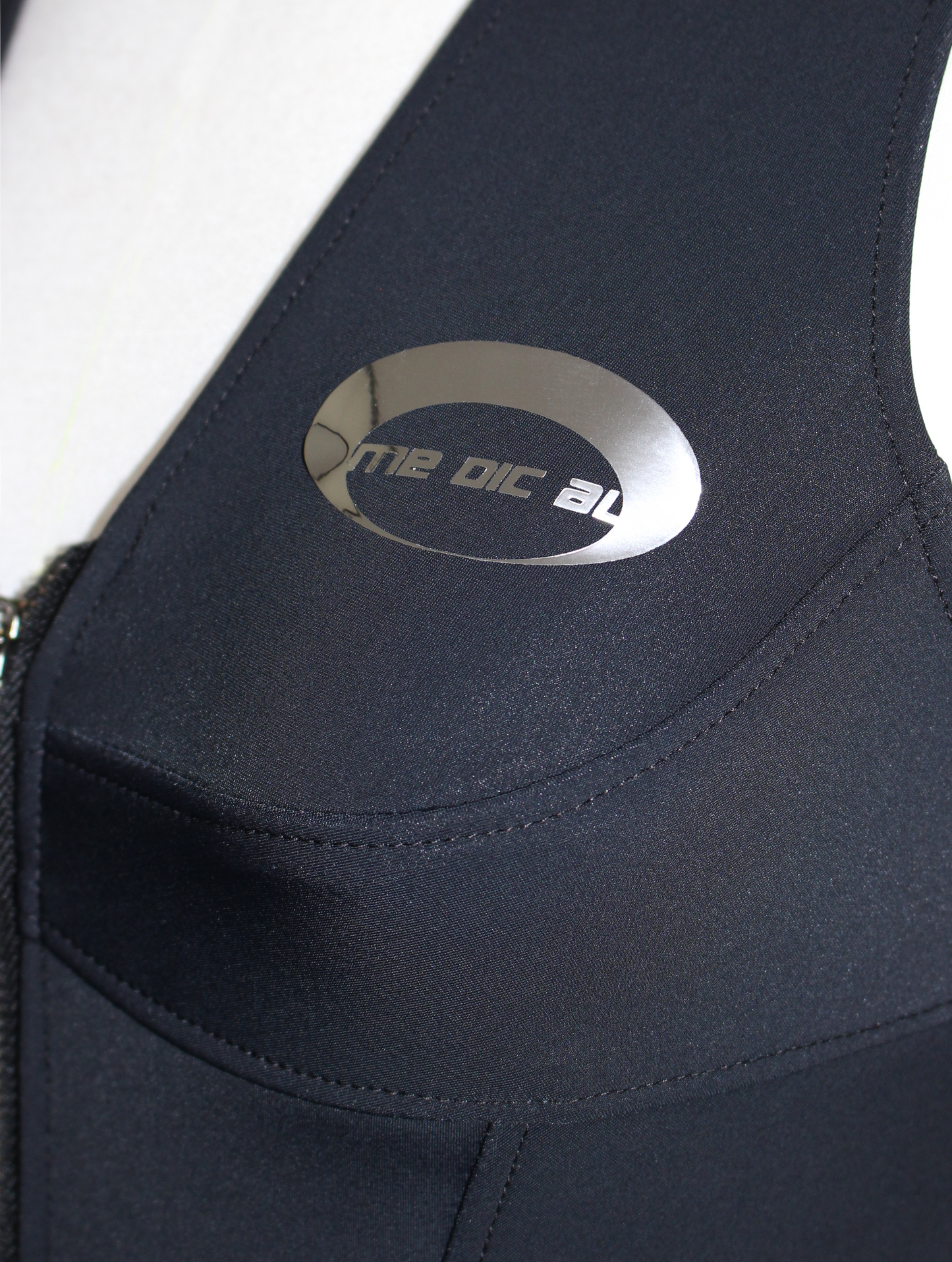 Detail shot of reflective metallic print that contains the me dic al logo and Black cyberpunk techwear vest with zipper front and futuristic design – urban streetwear crop top style for women in modern techwear fashion.